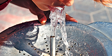 Eine Frau trinkt Wasser aus einem öffentlichen Brunnen.