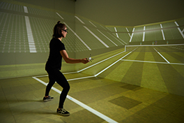 Zu sehen ist eine Frau in einem VR-Raum der aber aussieht wie ein virtueller Tennis-Platz und sie spielt virtuell